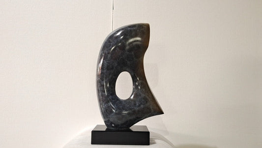 Abstract black marble sculpture on a white pedestal against a plain background