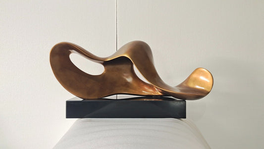 Abstract bronze sculpture on a black base against a neutral background