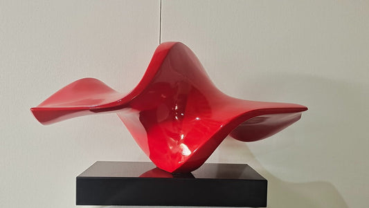 Red abstract sculpture on a black base against a white wall