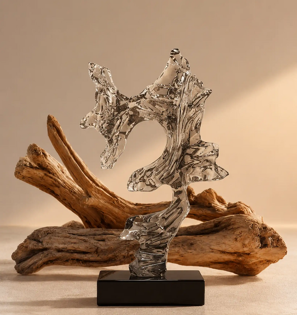 Abstract glass sculpture on a black base, with driftwood in the background