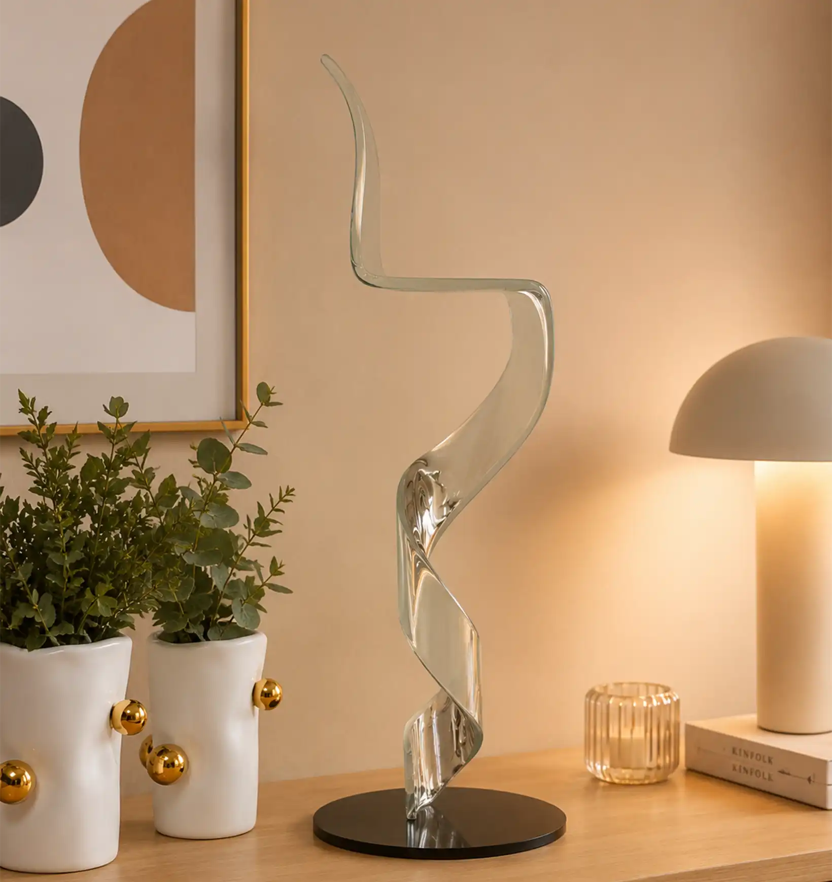 Clear acrylic spiral sculpture on a black base, next to two white vases with plants and a table lamp