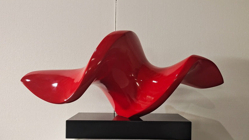 Red abstract sculpture on a black base against a plain background