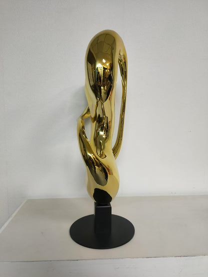 Gold abstract sculpture on a black stand against a white background