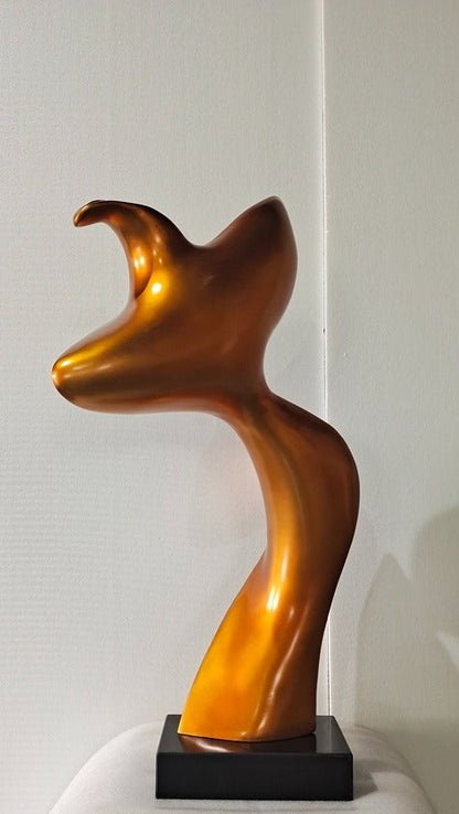 Abstract gold sculpture on a white surface with a light gray background