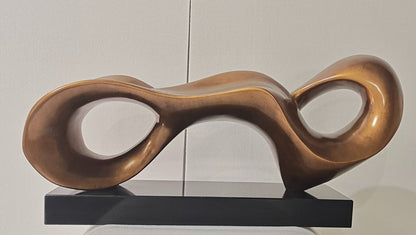 Bronze abstract sculpture on a black base against a white wall