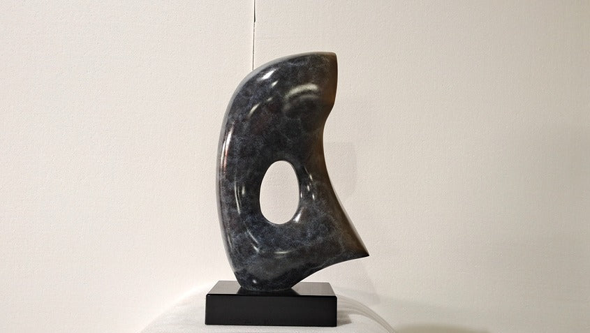 Abstract black marble sculpture on a white pedestal against a plain background