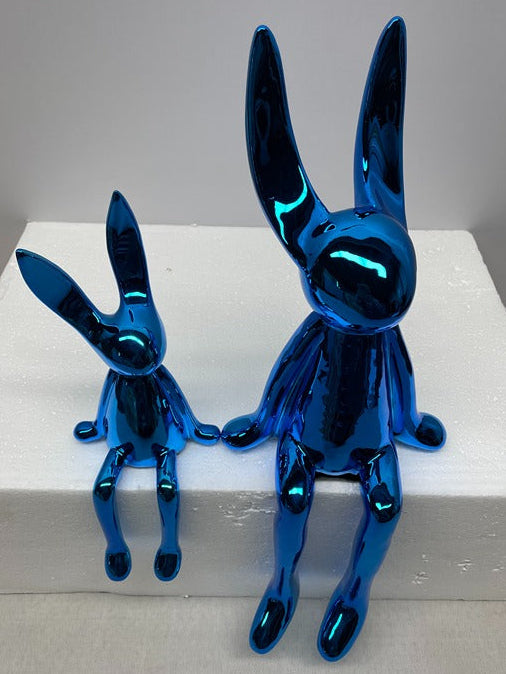 Two blue rabbit figurines on a white platform with a gray background