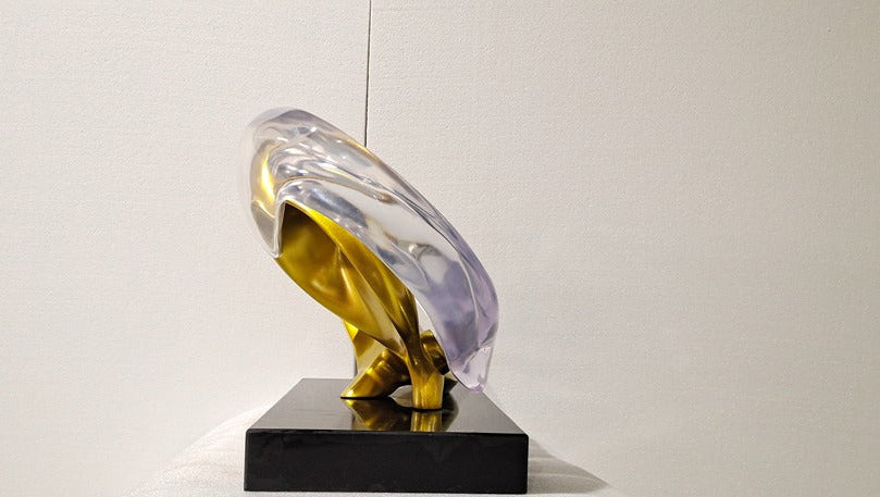 Modern sculpture with gold and clear acrylic elements on a black base against a white background