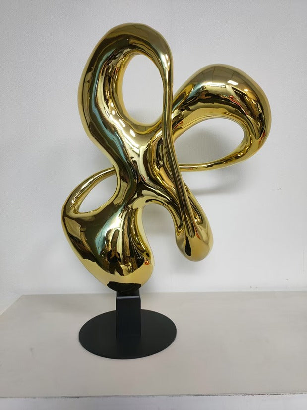Gold abstract sculpture on a black stand against a white background