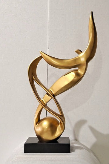 Gold abstract sculpture on a black base against a white wall