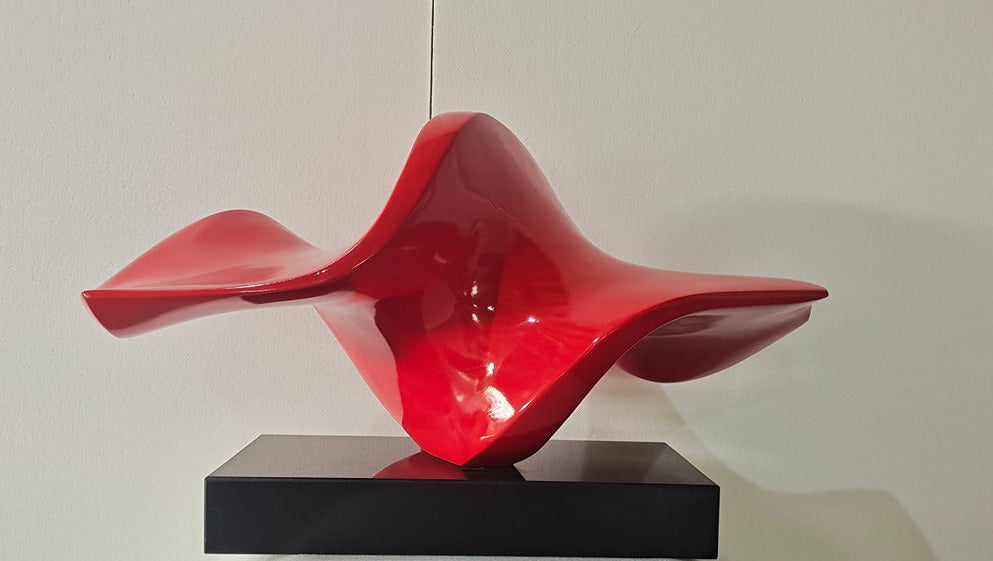 Red abstract sculpture on a black base against a white wall