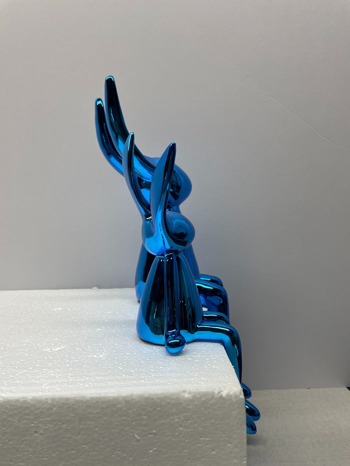 Blue metallic sculpture on a white surface with a gray background