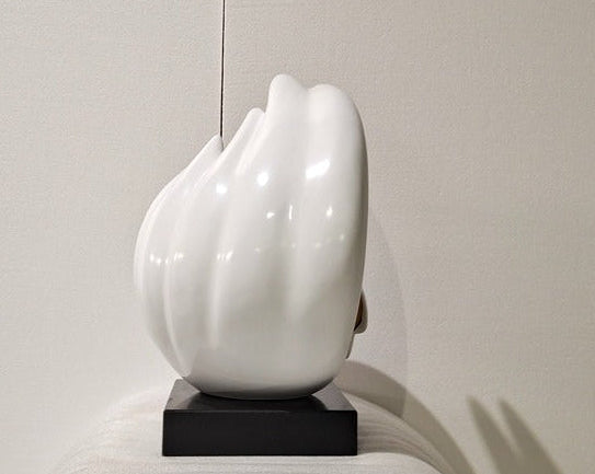 White ceramic sculpture on a black base against a neutral background