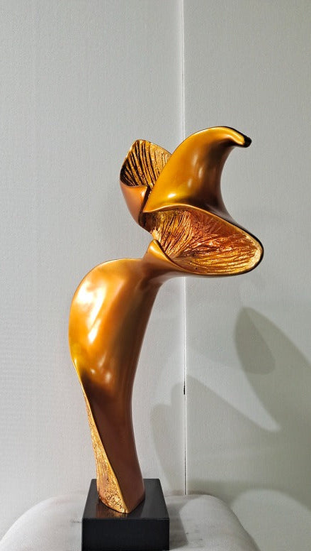 Gold abstract sculpture on a black base against a white wall