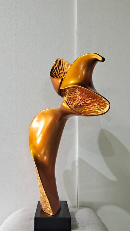 Gold abstract sculpture on a black base against a white wall