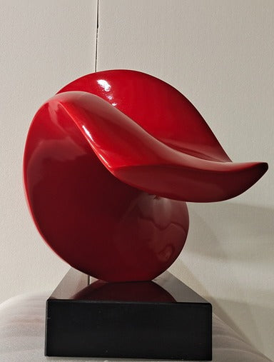 Red abstract sculpture on a black base against a neutral background