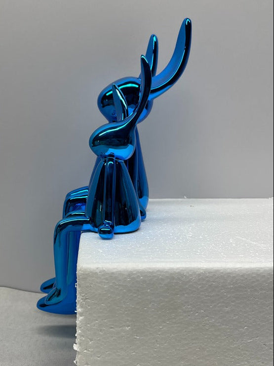 Blue metallic sculpture of a dog on a white surface with a gray background