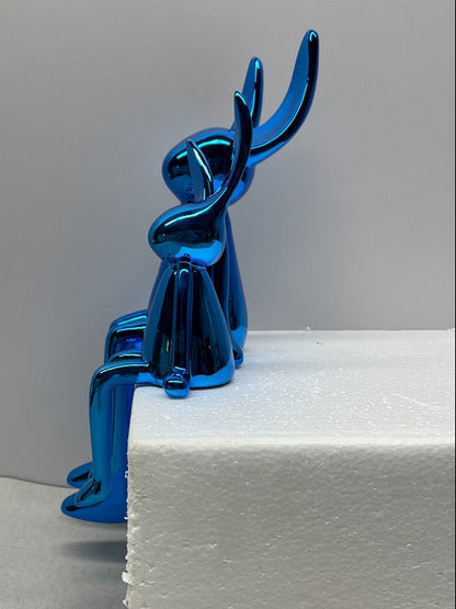 Blue metallic sculpture of a dog on a white surface with a gray background