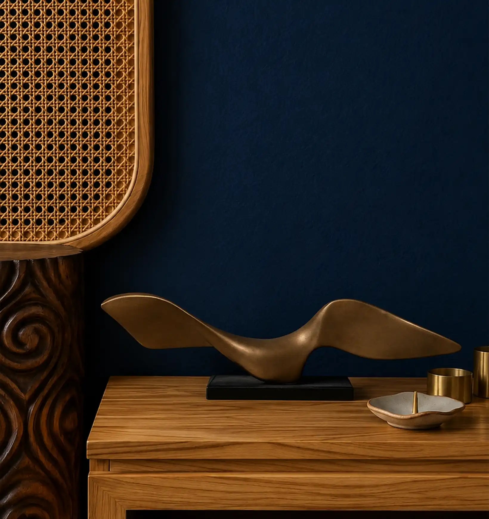 Bronze bird sculpture on a wooden dresser with a woven rattan screen and dark blue wall