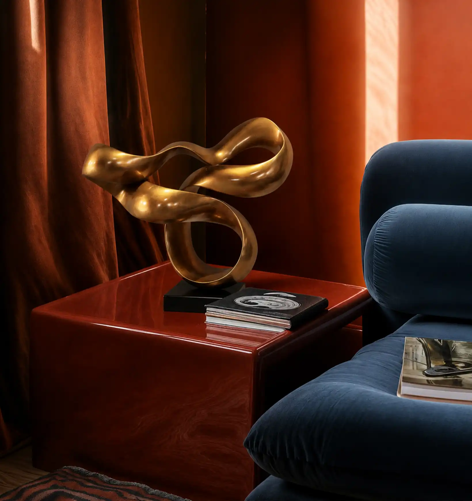 Bronze abstract sculpture on a red side table next to a blue velvet sofa