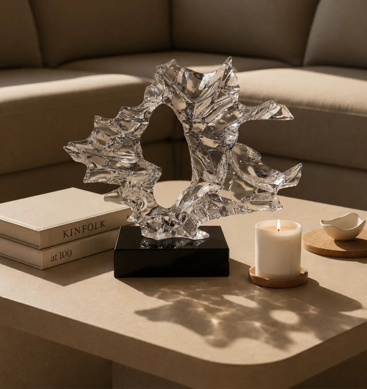 Abstract crystal sculpture on a black base, next to books and a lit candle on a coffee table