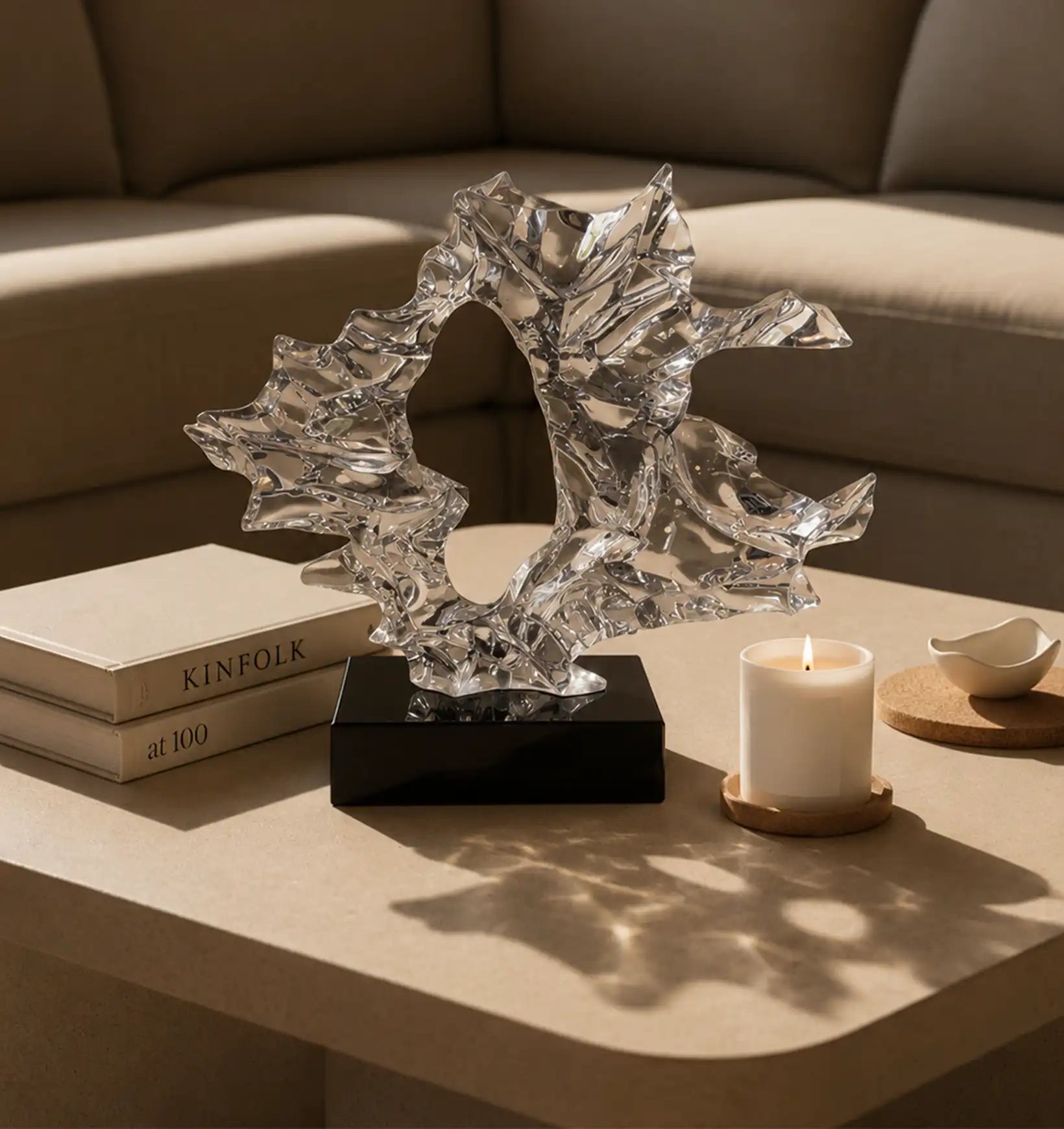 Abstract crystal sculpture on a black base, next to books and a lit candle on a coffee table