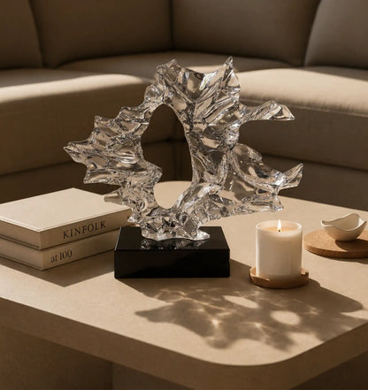 Abstract crystal sculpture on a black base, next to books and a lit candle on a coffee table