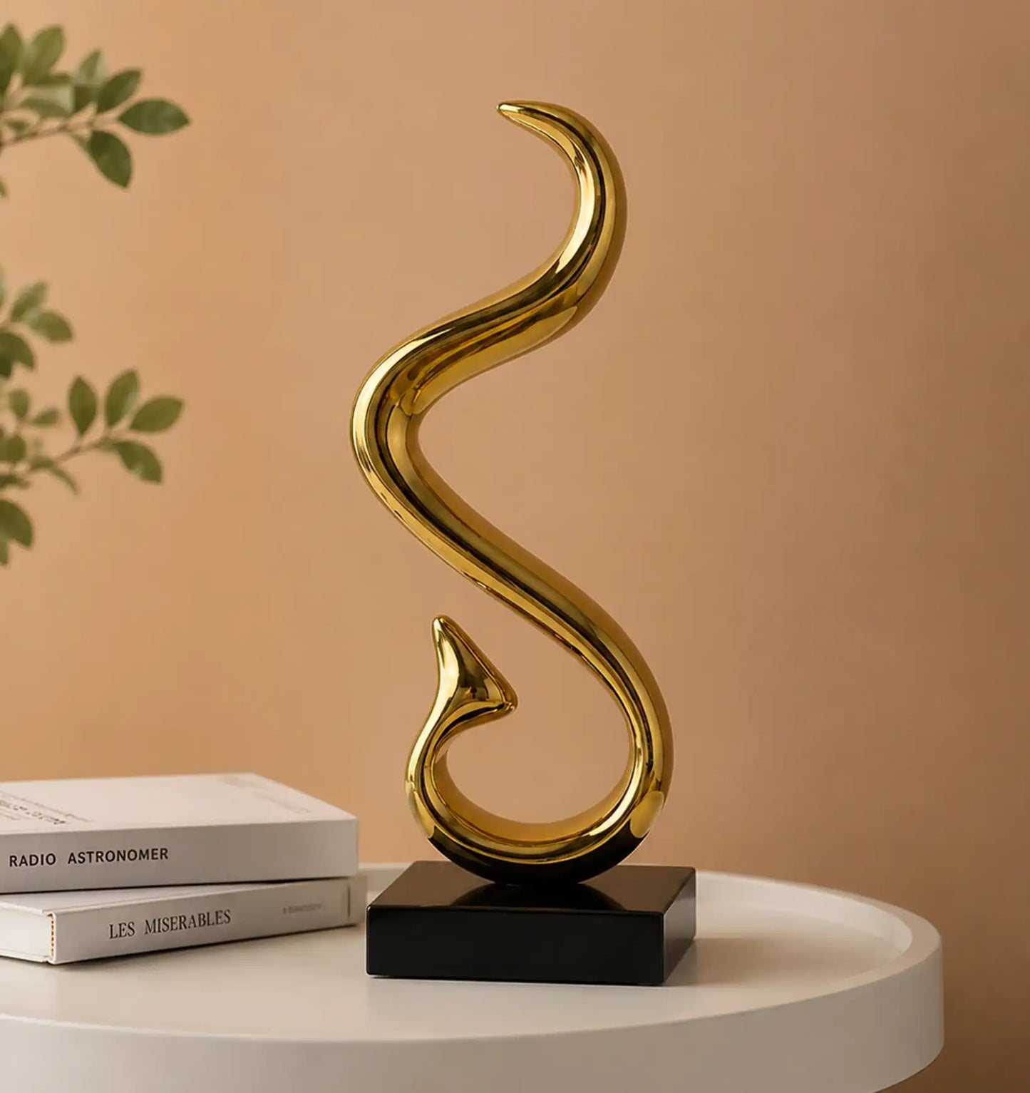 Gold abstract sculpture on a black base, with two books and a plant in the background