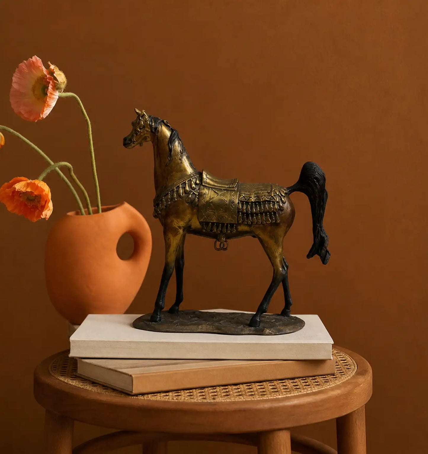 Bronze horse figurine with saddle and tassels, next to a terracotta vase with orange poppies