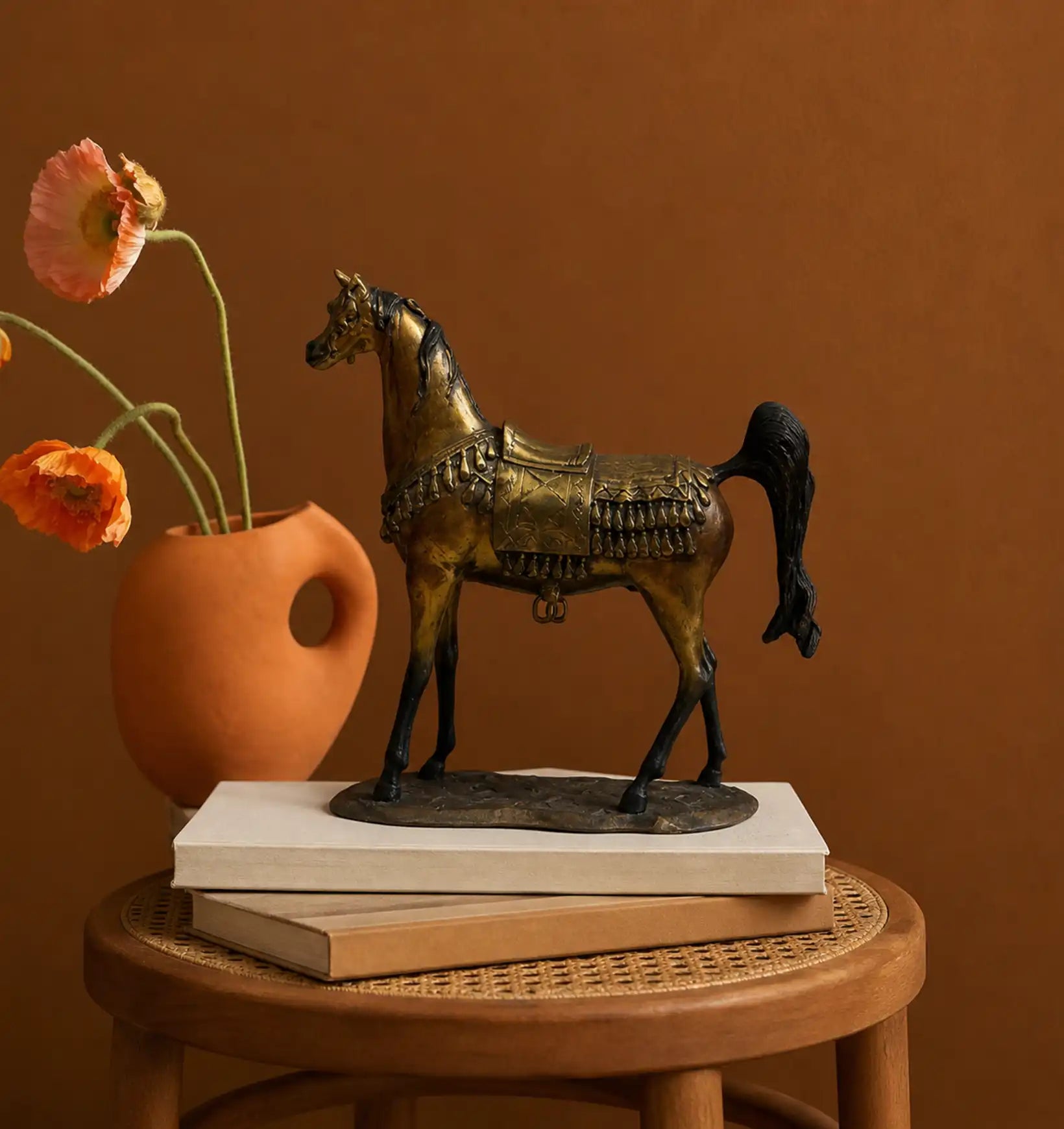 Bronze horse figurine with saddle and tassels, next to a terracotta vase with orange poppies