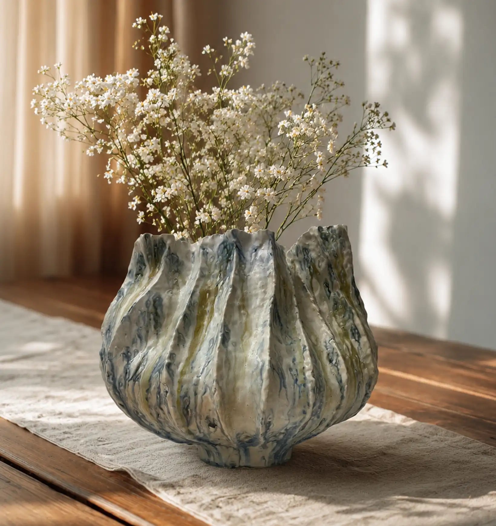 White baby's breath flowers in a blue and green marbled ceramic vase on a wooden table