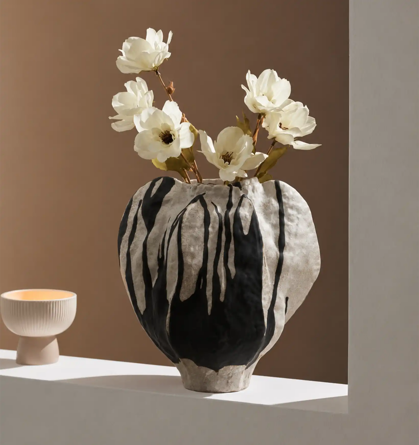 White flowers in a black and white vase, with a small beige bowl next to it