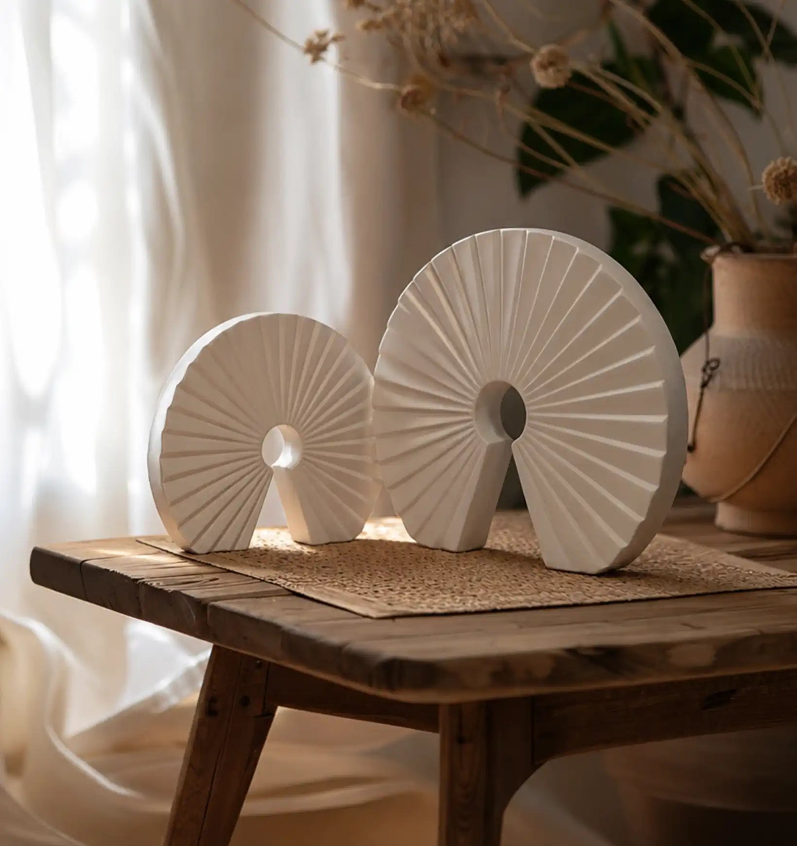 Two white decorative fan-shaped objects with a circular cutout on a wooden table