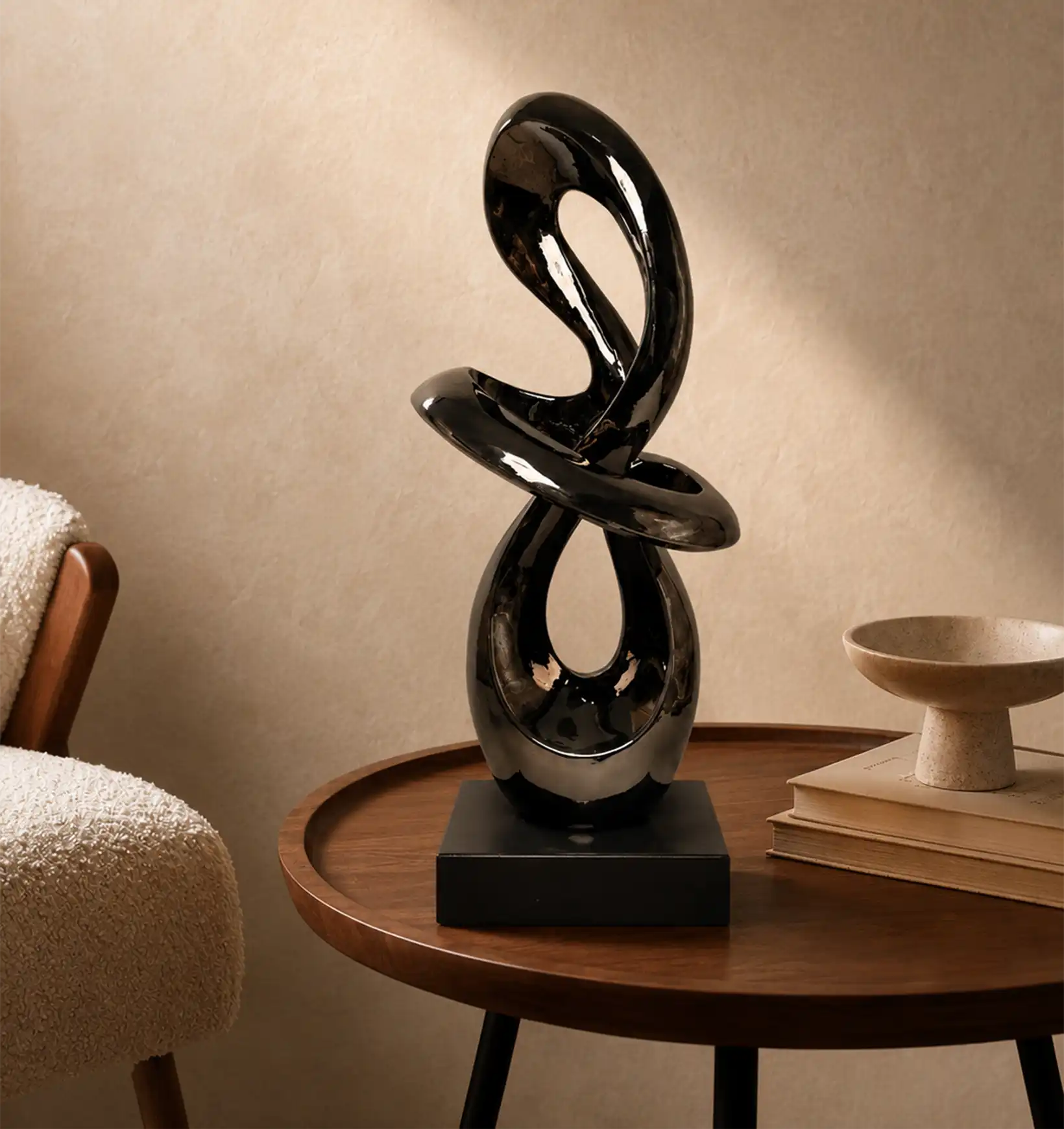 Black abstract sculpture on a wooden side table next to a cream chair and books
