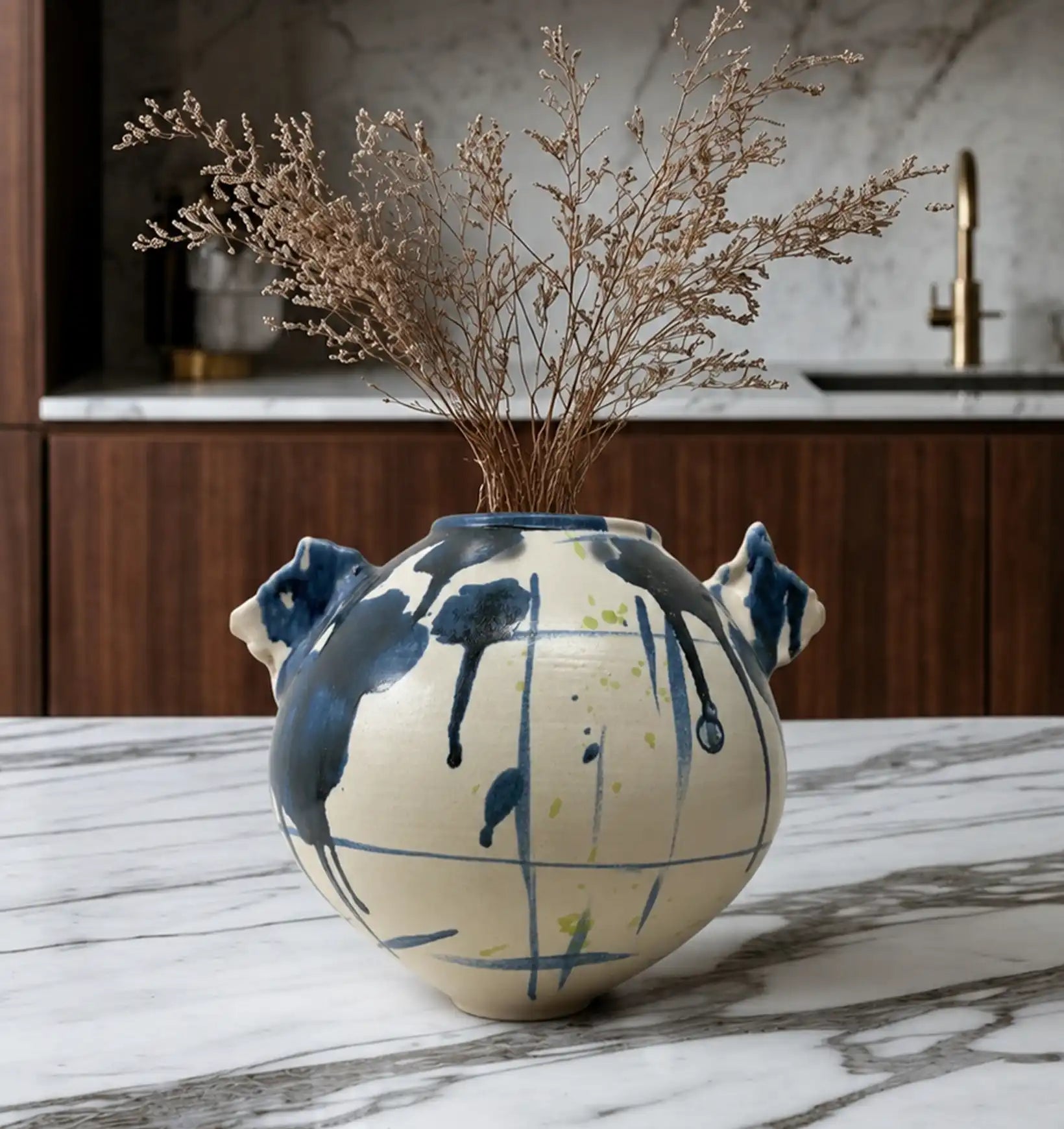 Ceramic vase with blue and yellow abstract design, holding dried flowers on a marble counter